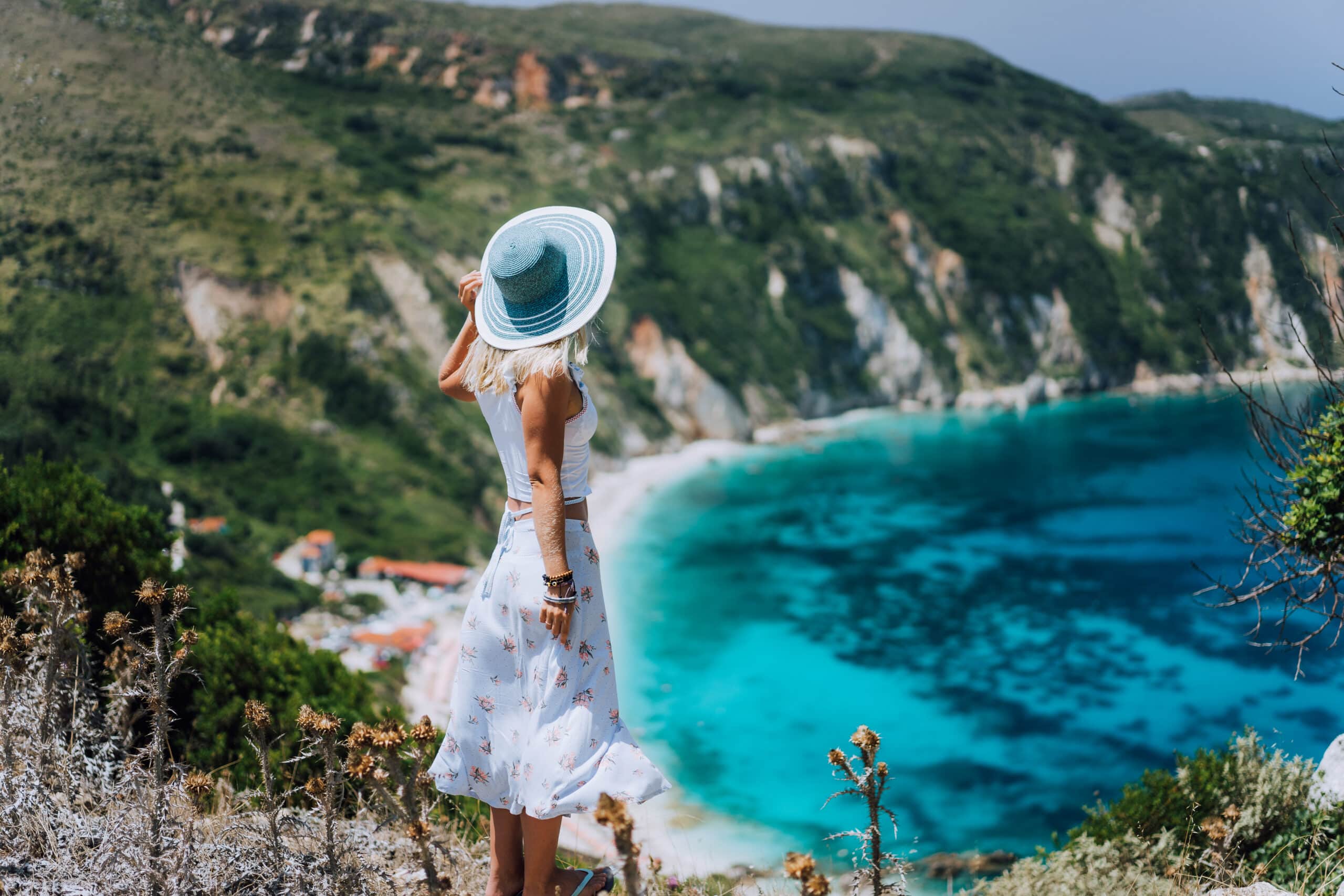 Young woman on Petani beach Kefalonia, admiring highly excited picturesque panorama of emerald blue bay of Mediterranean sea and steep coastline hills. Greece.
